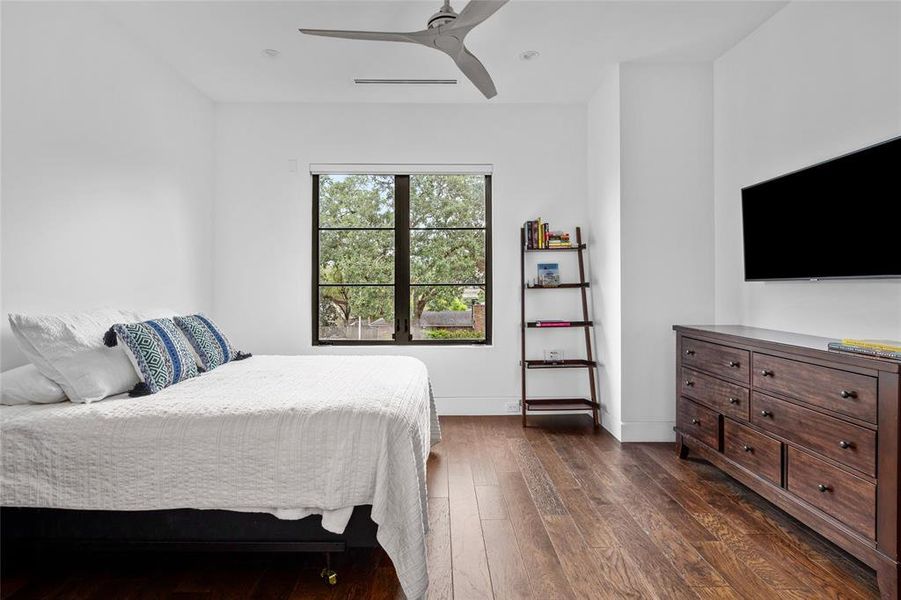 This secondary bedroom showcases rich hardwood floors and large windows, offering plenty of natural light. The room is designed with clean, minimalistic lines and features a ceiling fan for added comfort.