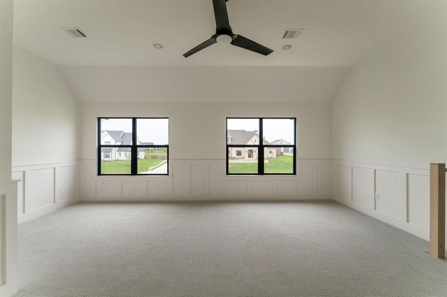Spare room with a decorative wall, vaulted ceiling, plenty of natural light, light colored carpet, and a wainscoted wall Spare room with a decorative wall, vaulted ceiling, plenty of natural light, light colored carpet, and a wainscoted wall