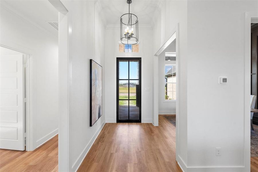 Foyer entrance with light wood finished floors, ornamental molding, and a chandelier