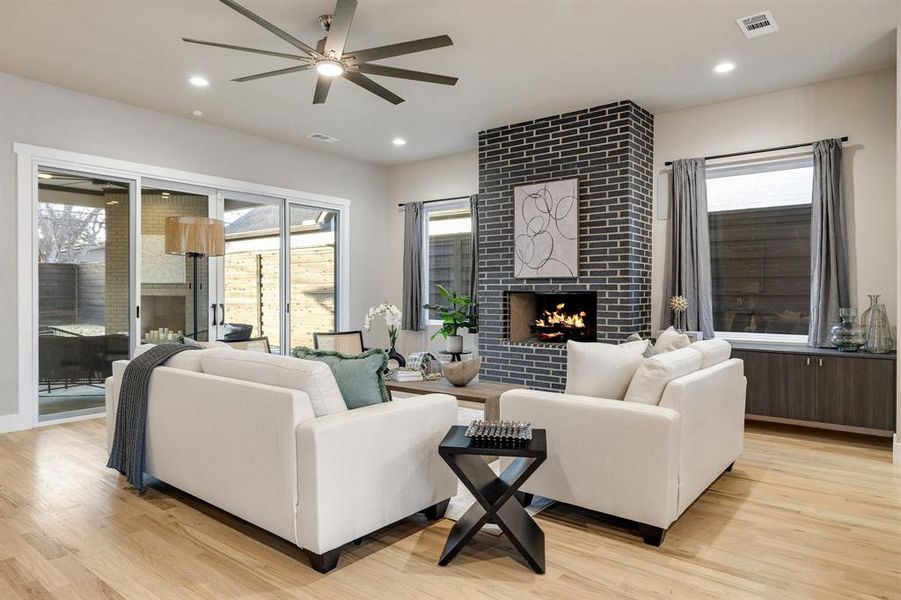 Living room with a large fireplace, ceiling fan, and light hardwood / wood-style floors