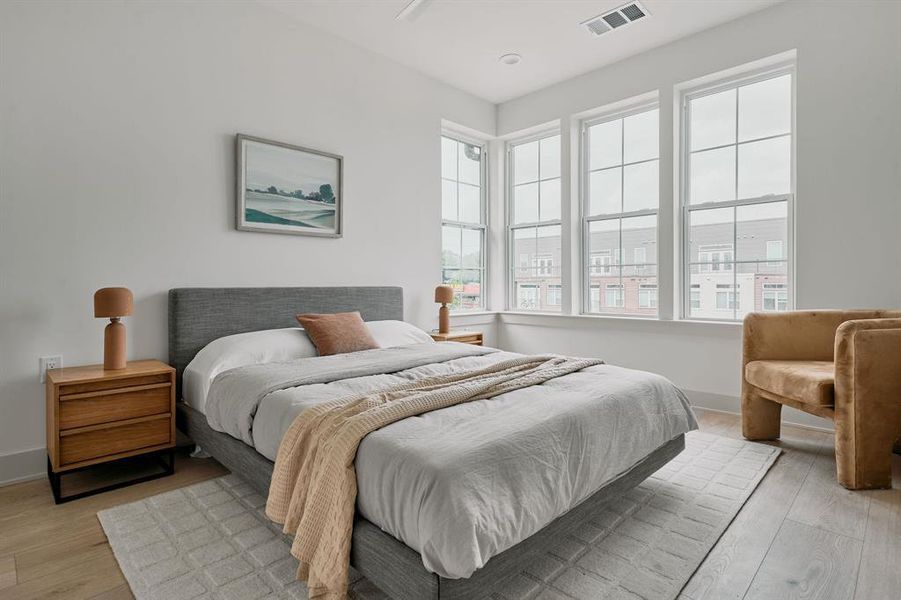 Corner bedroom featuring extensive natural light from multiple large windows, light wood-finish flooring, and crisp white walls Corner bedroom featuring extensive natural light from multiple large windows, light wood-finish flooring, and crisp white walls