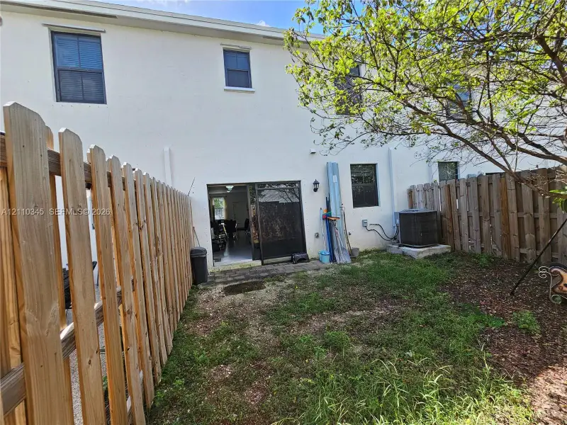 Stucco exterior rear elevation featuring a sliding glass door, enclosed private yard with vertical wood privacy fencing, and exterior lighting