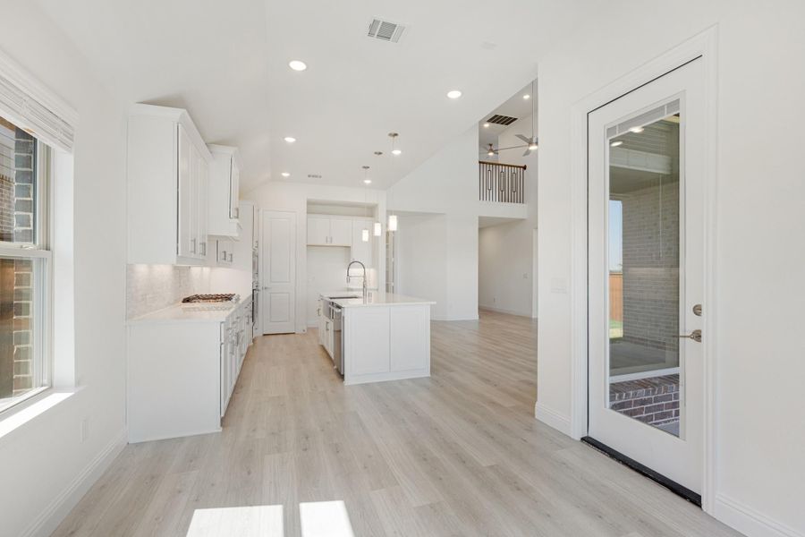 Open kitchen with white cabinets, center island, light wood floors, and glass door to patio Open kitchen with white cabinets, center island, light wood floors, and glass door to patio