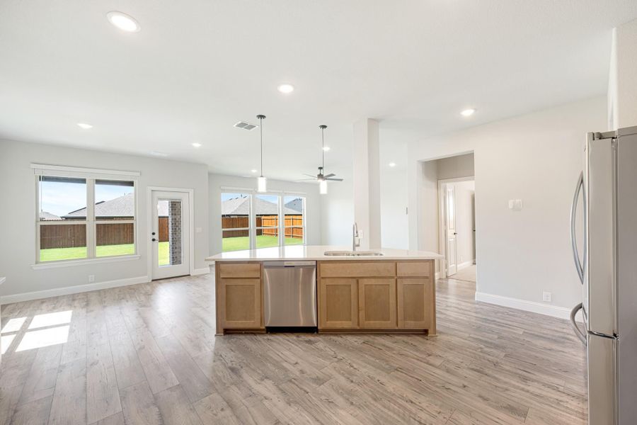 Open kitchen with large island, light wood cabinets, stainless appliances, and hardwood floors opening to living area