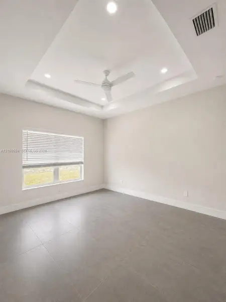 Tray ceiling featuring a central white ceiling fan, recessed lighting, and large-format tile flooring