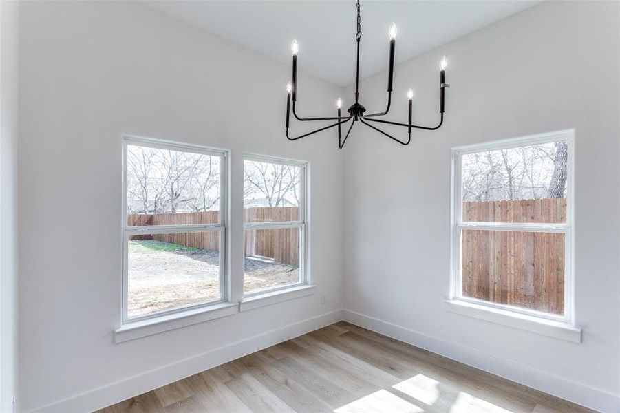 Unfurnished dining area with a notable chandelier, light wood finished floors, and baseboards