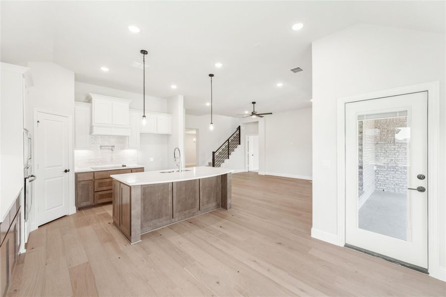 Open kitchen with large island, white upper cabinets, wood lower cabinets, pendant lights, and light hardwood floors