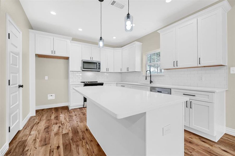 Kitchen with a center island, stainless steel appliances, pendant lighting, white cabinets, and light wood-type flooring