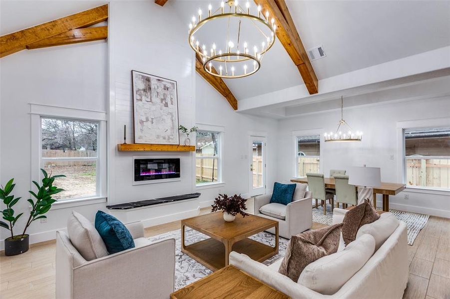 Living room featuring a notable chandelier, a wealth of natural light, beamed ceiling, and light wood-type flooring