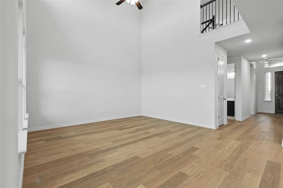 Unfurnished room with a ceiling fan, light wood-style flooring, baseboards, and a towering ceiling Unfurnished room with a ceiling fan, light wood-style flooring, baseboards, and a towering ceiling