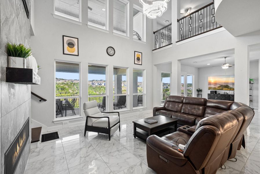 Living room with a tiled fireplace, a chandelier, light marble finish floors, and a ceiling fan