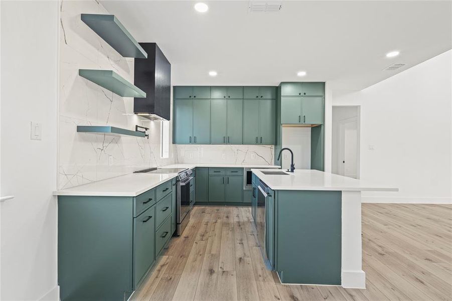 Kitchen featuring green cabinetry, open shelves, light stone countertops, tasteful backsplash, and appliances with stainless steel finishes