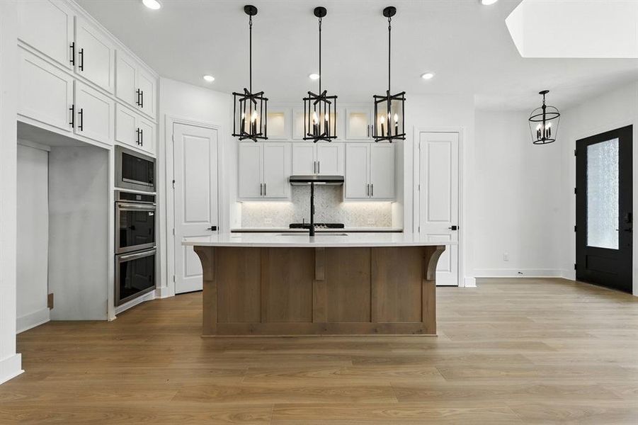 Kitchen featuring decorative light fixtures, a center island with sink, tasteful backsplash, light wood-style floors, and a kitchen bar Kitchen featuring decorative light fixtures, a center island with sink, tasteful backsplash, light wood-style floors, and a kitchen bar
