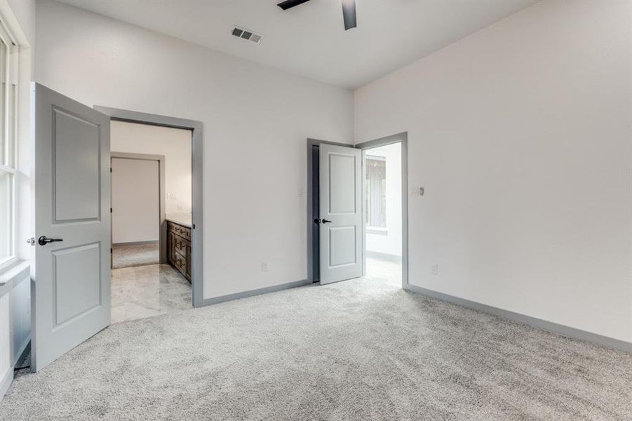 Unfurnished bedroom with ensuite bath, ceiling fan, and light carpet