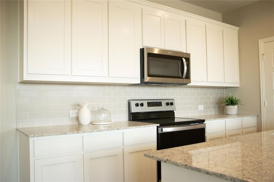 Kitchen featuring white cabinetry, light stone counters, tasteful backsplash, and stainless steel appliances