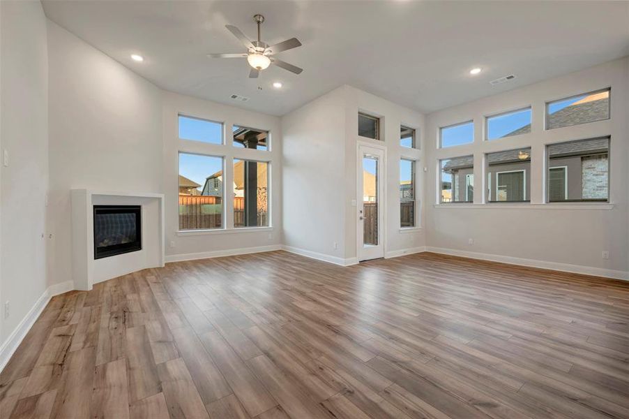 Unfurnished living room with a high ceiling, ceiling fan, a glass covered fireplace, light wood finished floors, and recessed lighting