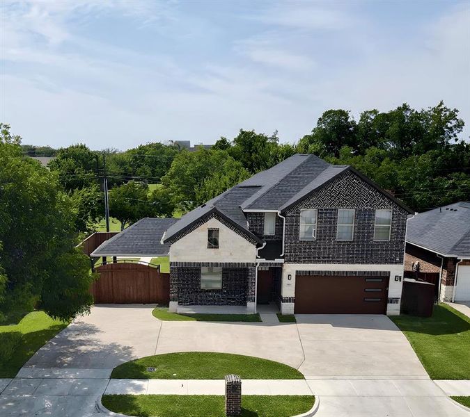 View of front facade with curved driveway, brick siding, a garage, and view of scattered trees