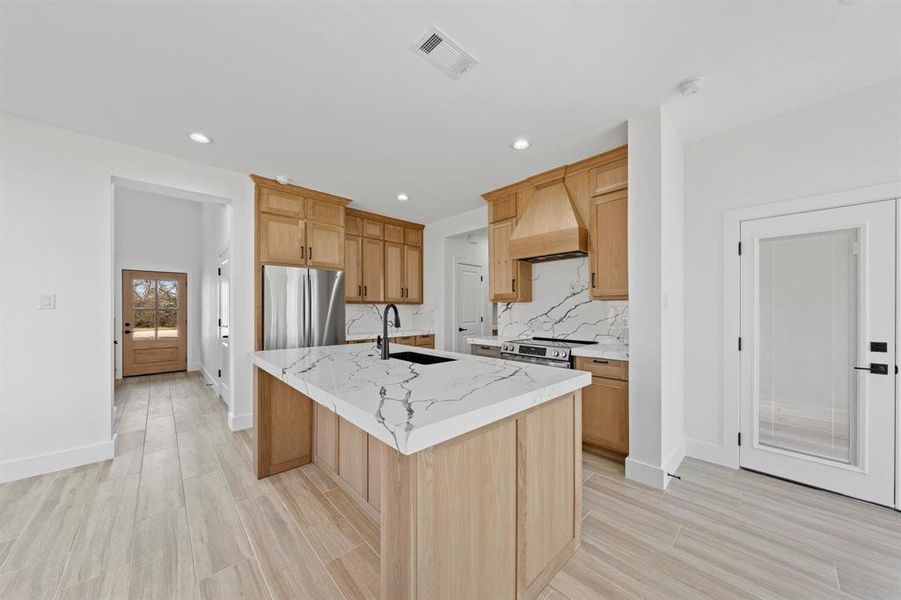 Kitchen featuring a kitchen island with sink, a sink, visible vents, appliances with stainless steel finishes, and custom exhaust hood