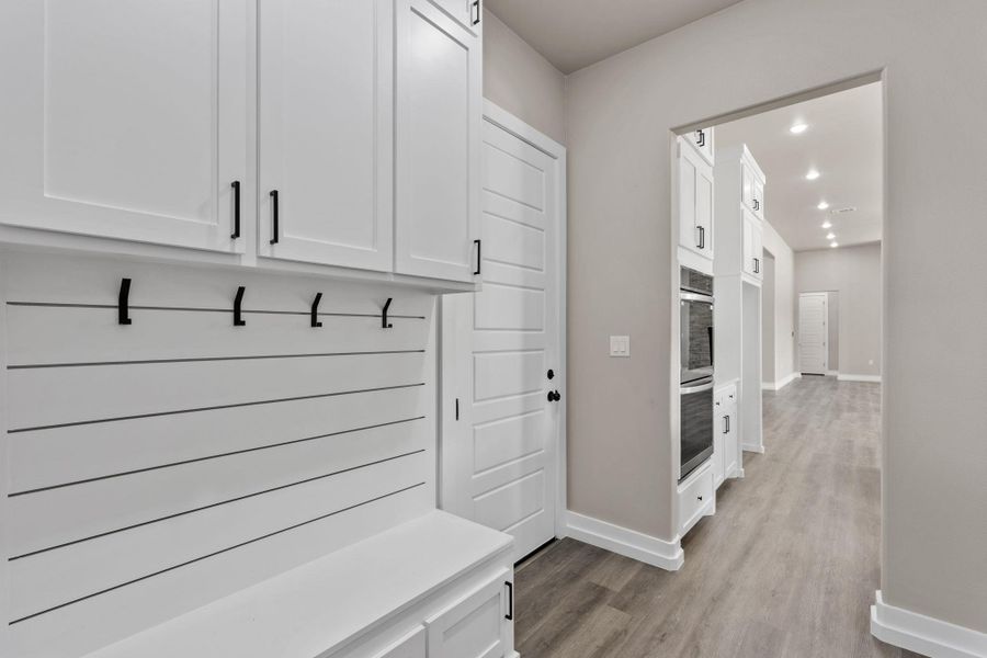 Functional mudroom with built-in bench and storage connects to a sleek hallway featuring integrated double ovens. Functional mudroom with built-in bench and storage connects to a sleek hallway featuring integrated double ovens.