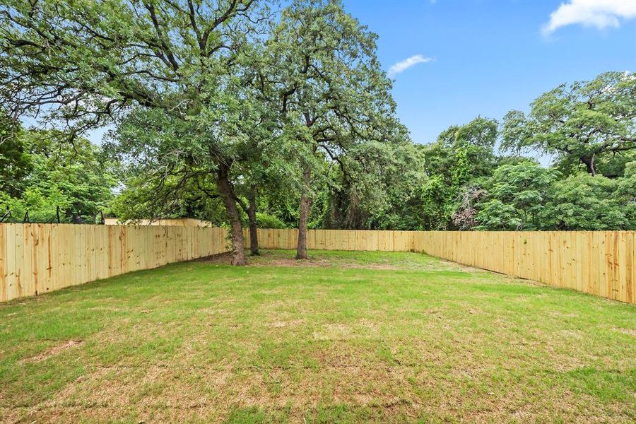 Spacious backyard featuring a manicured lawn, new wood fencing, and mature trees