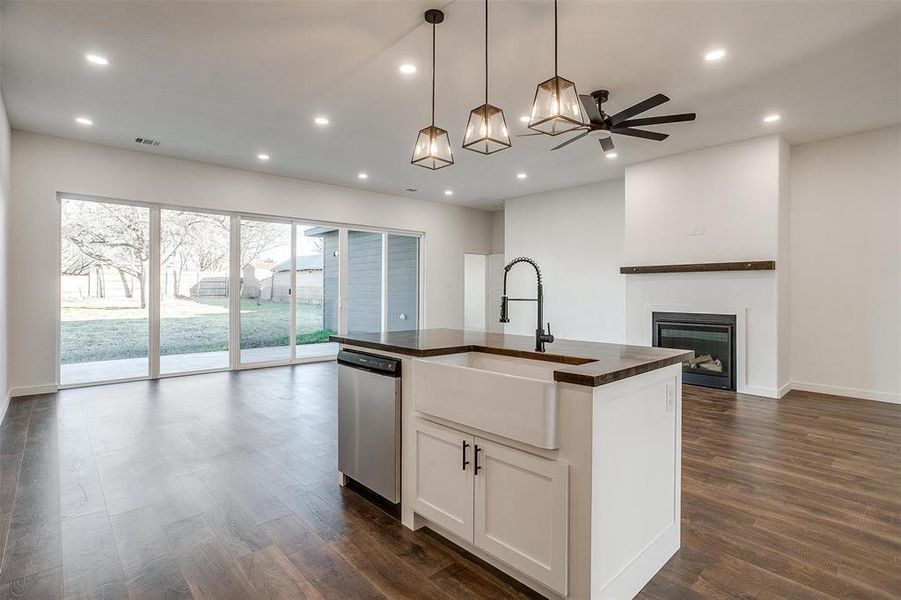 Kitchen featuring dishwasher, a center island with sink, hanging light fixtures, sink, and white cabinetry