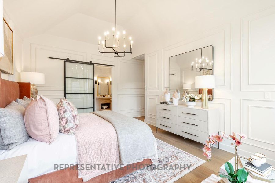 Bedroom with a decorative wall, a chandelier, a barn door, light wood-type flooring, and vaulted ceiling Bedroom with a decorative wall, a chandelier, a barn door, light wood-type flooring, and vaulted ceiling