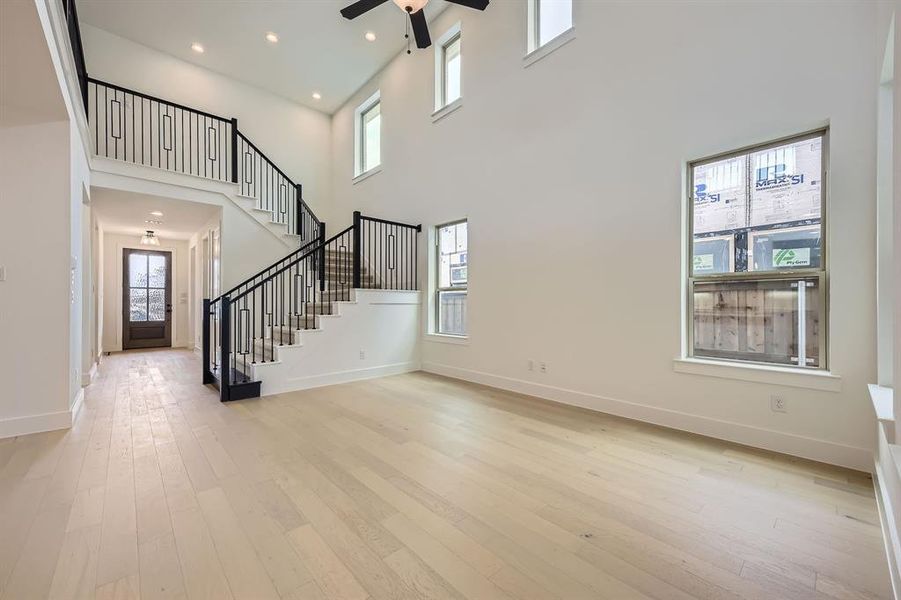 Unfurnished living room featuring a high ceiling, a ceiling fan, stairs, hardwood / wood-style flooring, and recessed lighting Unfurnished living room featuring a high ceiling, a ceiling fan, stairs, hardwood / wood-style flooring, and recessed lighting