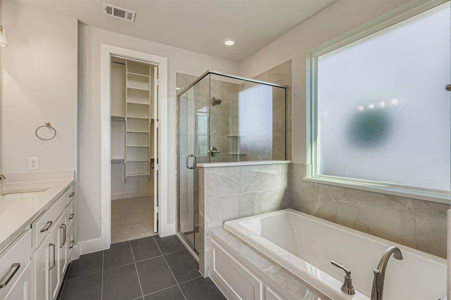 Full bath featuring vanity, a garden tub, a walk in closet, dark tile patterned flooring, and a shower stall