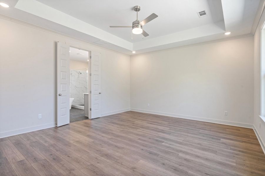 Unfurnished bedroom featuring recessed lighting, a tray ceiling, a ceiling fan, dark wood-style floors, and connected bathroom