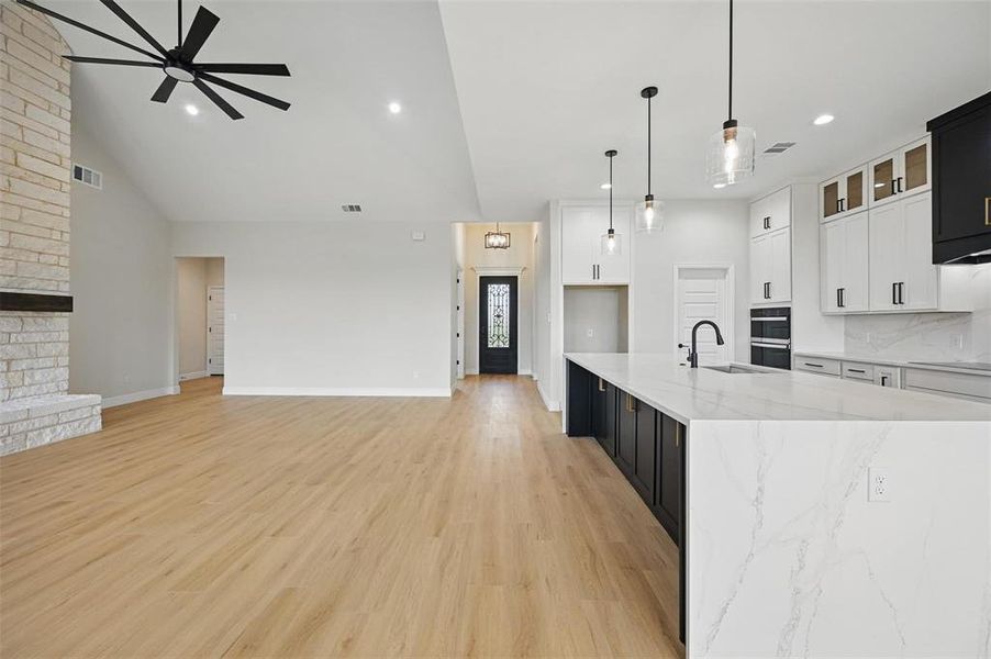 Kitchen with dark cabinetry, white cabinetry, hanging light fixtures, light stone counters, and light wood-type flooring Kitchen with dark cabinetry, white cabinetry, hanging light fixtures, light stone counters, and light wood-type flooring