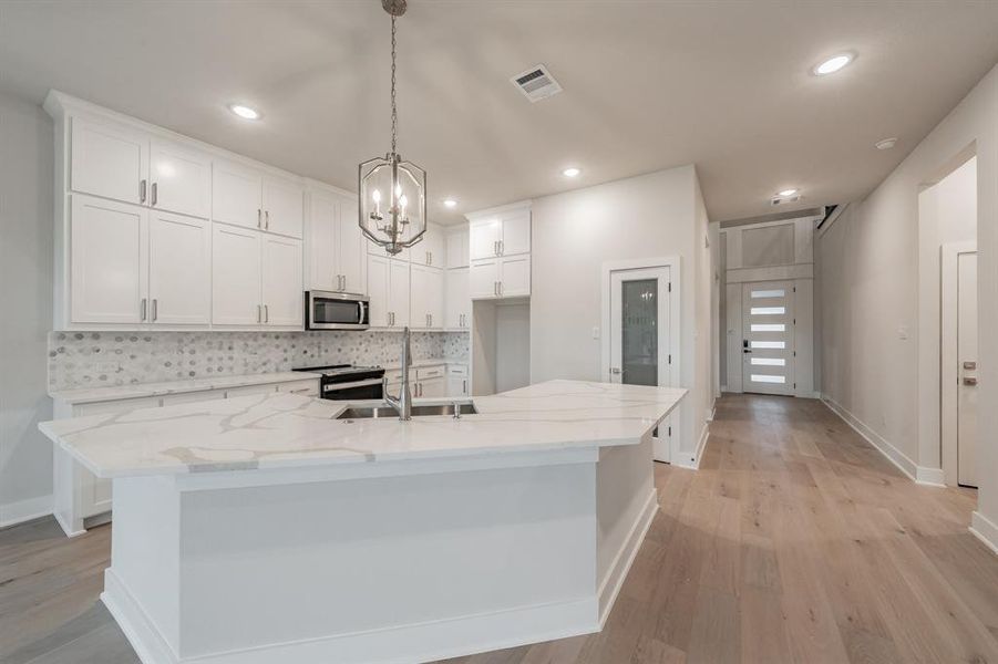 Kitchen with white cabinetry, light stone countertops, backsplash, a large island, and electric stove