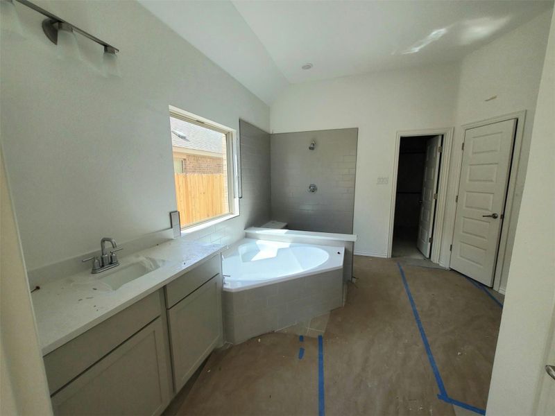 Bathroom featuring tiled shower, tiled tub, lofted ceiling, and vanity