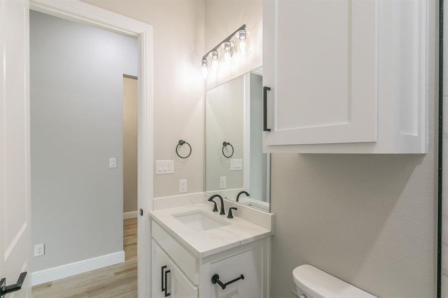 Bathroom featuring vanity, toilet, wood finished floors, and baseboards Bathroom featuring vanity, toilet, wood finished floors, and baseboards