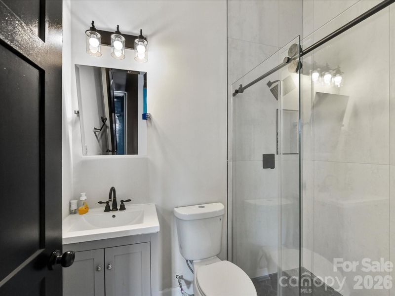 Clean and modern ensuite bathroom featuring a sleek vanity, updated lighting, and a glass-enclosed shower.
