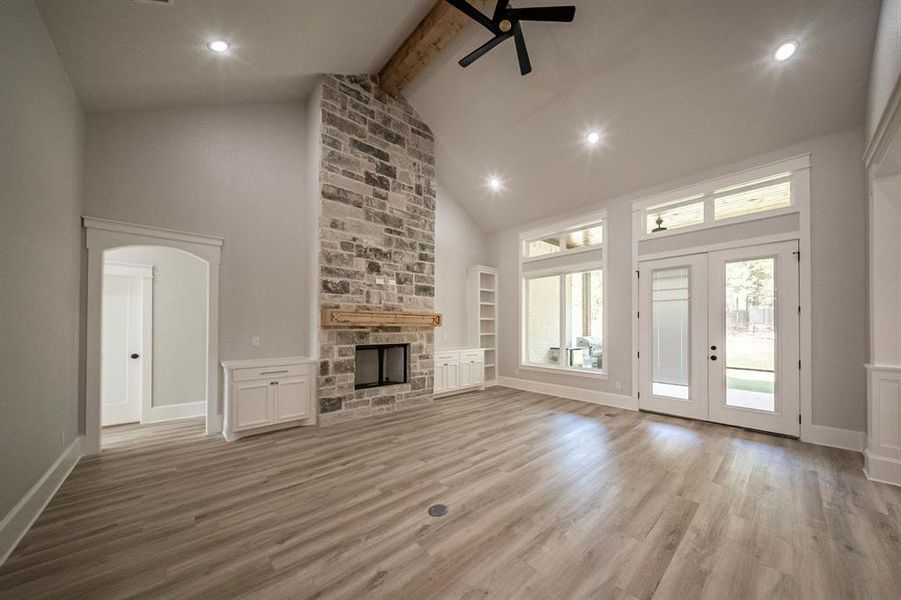 Unfurnished living room with beam ceiling, recessed lighting, a stone fireplace, high vaulted ceiling, and french doors Unfurnished living room with beam ceiling, recessed lighting, a stone fireplace, high vaulted ceiling, and french doors