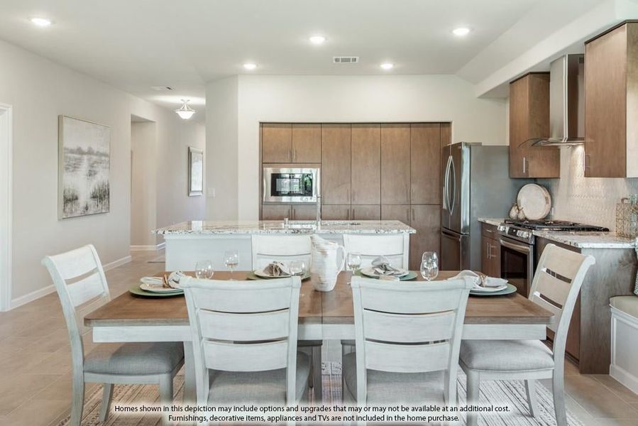 Open dining area with wood table and white chairs adjacent to kitchen with dark cabinets and stainless steel appliances