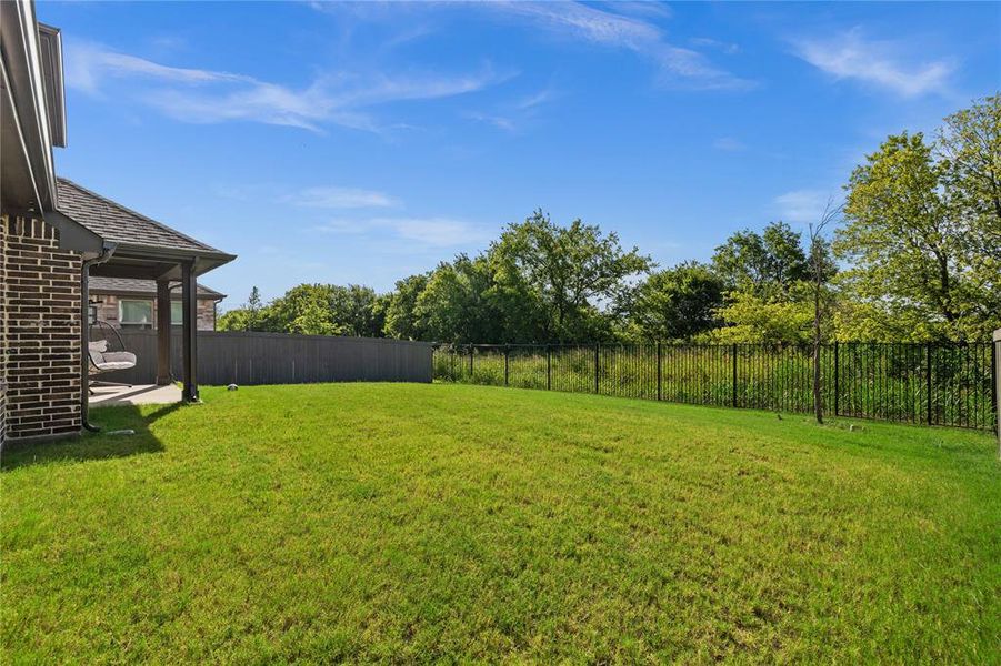 Expansive green lawn with a covered patio, brick exterior, and a combination privacy and wrought iron fencing