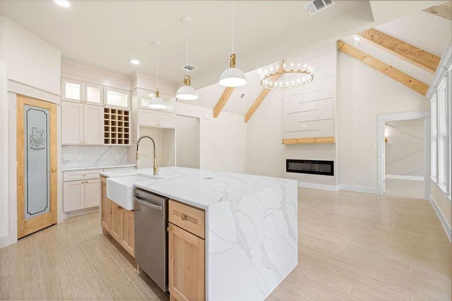 Kitchen featuring visible vents, stainless steel dishwasher, a glass covered fireplace, a sink, and beamed ceiling