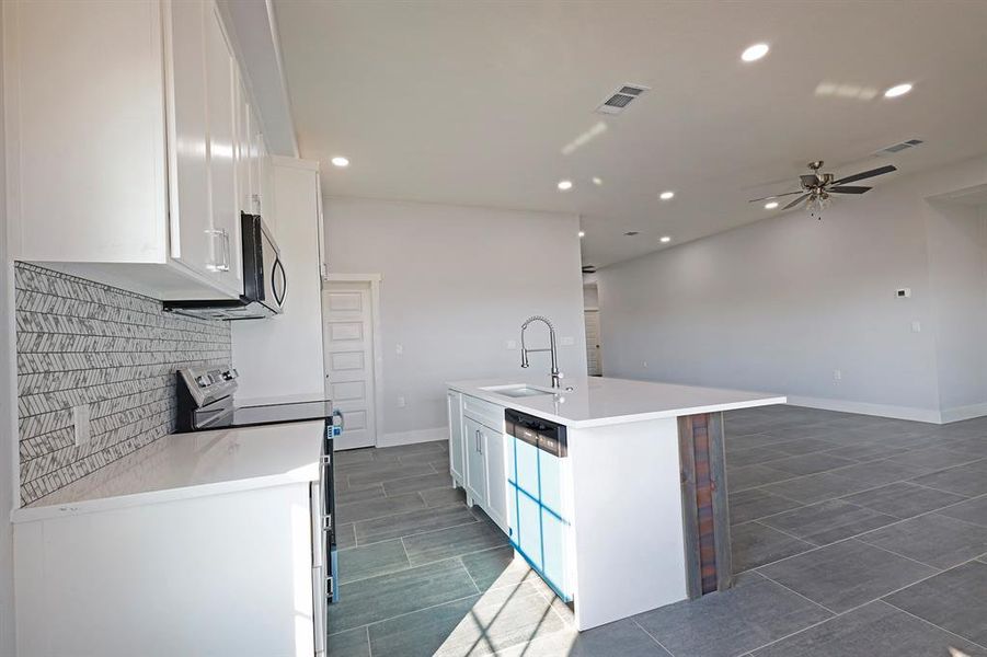 Kitchen with appliances with stainless steel finishes, white cabinets, recessed lighting, tasteful backsplash, and a center island with sink Kitchen with appliances with stainless steel finishes, white cabinets, recessed lighting, tasteful backsplash, and a center island with sink