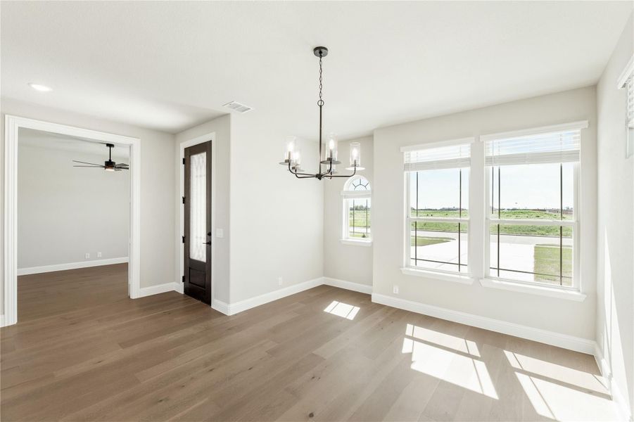 Empty dining room with hardwood floors, chandelier, and large windows overlooking a yard Empty dining room with hardwood floors, chandelier, and large windows overlooking a yard