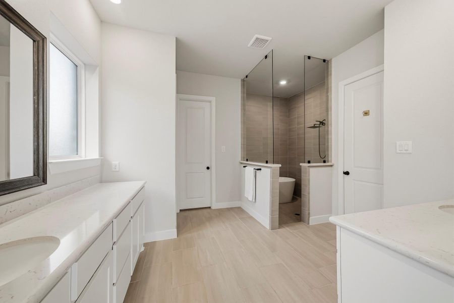 The primary bath showcases sophisticated 12" x 24" tile flooring and dual Quartz-topped vanities, complemented by framed mirrors and recessed lighting for a crisp, upscale finish. Straight ahead is a walk-in closet with access to the utility room and a water closet is hidden on the left.