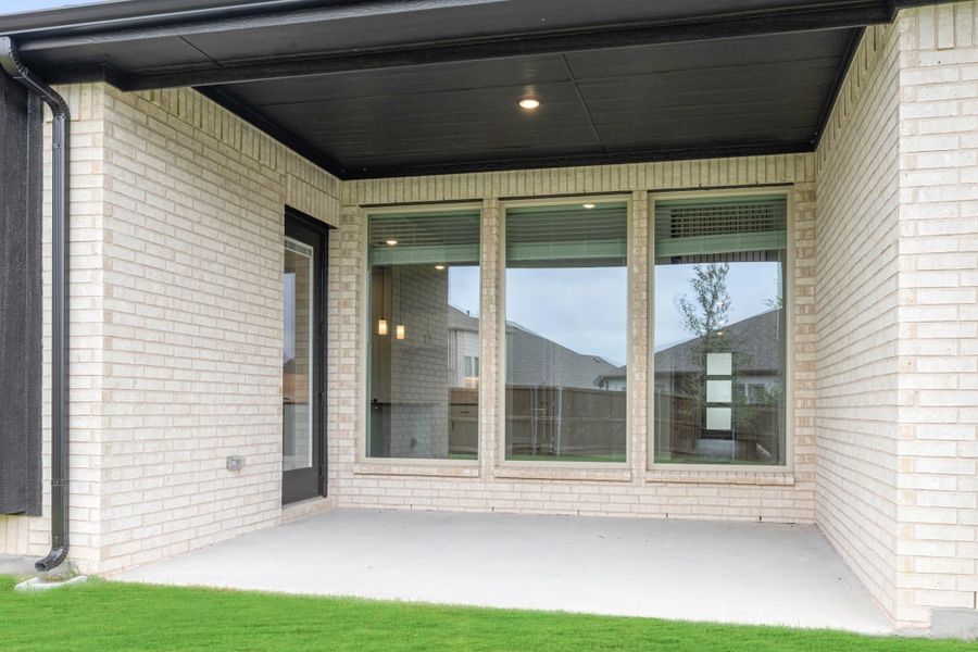Covered back patio with light brick walls, large windows, and concrete floor next to green lawn Covered back patio with light brick walls, large windows, and concrete floor next to green lawn