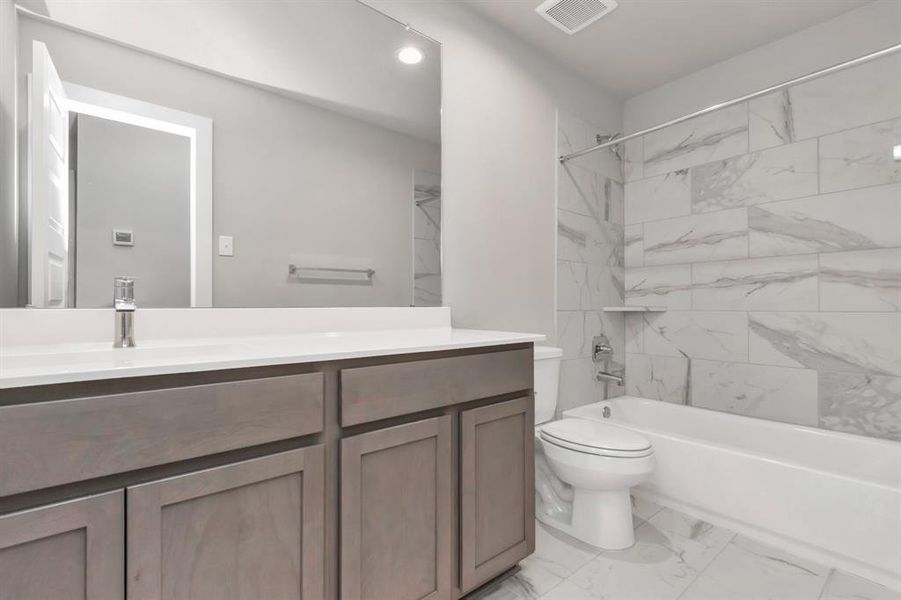 Indulge in refined charm in the secondary bathroom, where the tile flooring harmonizes with a bath/shower combo surrounded by tasteful tile. Light wood cabinets, coupled with a gorgeous countertop, elevate the space, cultivating a truly welcoming atmosphere. Sample photo of completed home with similar floor plan. As-built interior colors and selections may vary.