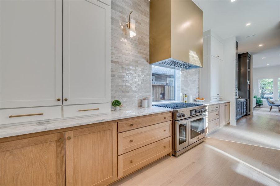 Kitchen featuring wall chimney exhaust hood, light hardwood / wood-style floors, light brown cabinetry, double oven range, and white cabinetry