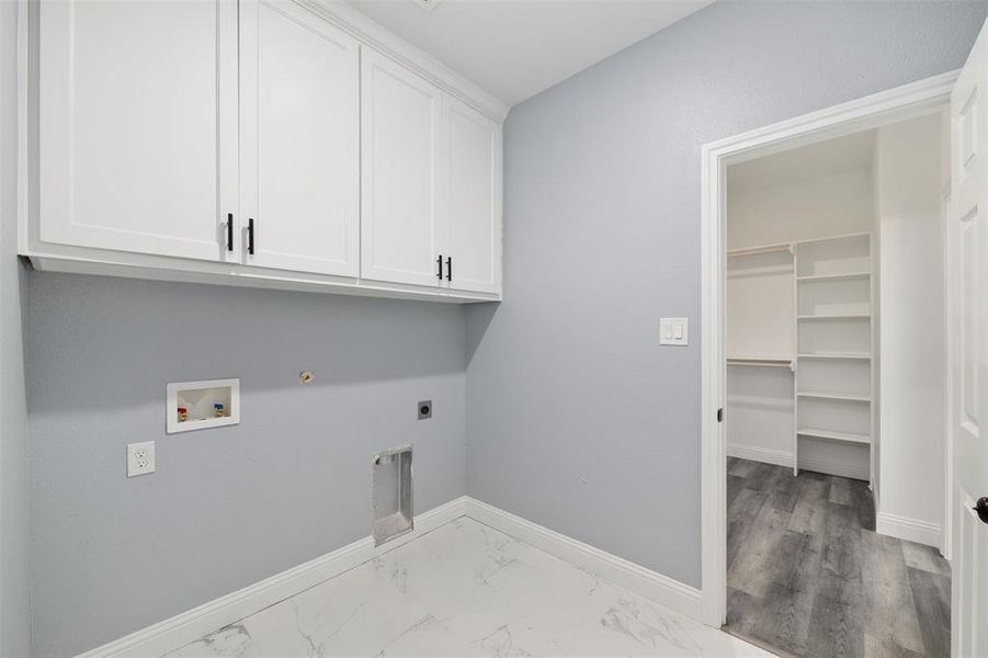 Laundry area featuring hookup for a gas dryer, electric dryer hookup, washer hookup, marble look tiles, and cabinet space Laundry area featuring hookup for a gas dryer, electric dryer hookup, washer hookup, marble look tiles, and cabinet space