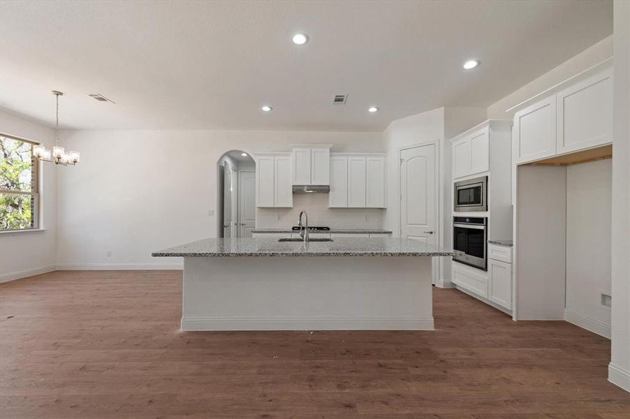 Kitchen with an island with sink, appliances with stainless steel finishes, white cabinetry, light stone countertops, and hardwood / wood-style flooring