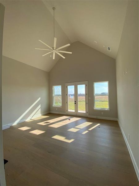 Unfurnished room with high vaulted ceiling, a ceiling fan, wood finished floors, and french doors
