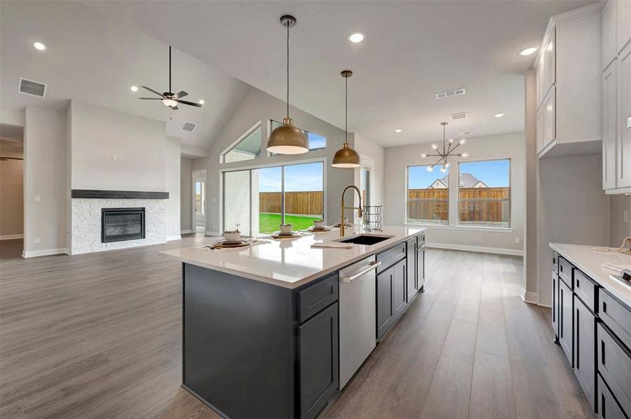 Open-concept kitchen featuring a large island with a sink and pendant lighting, white countertops, and dark cabinetry