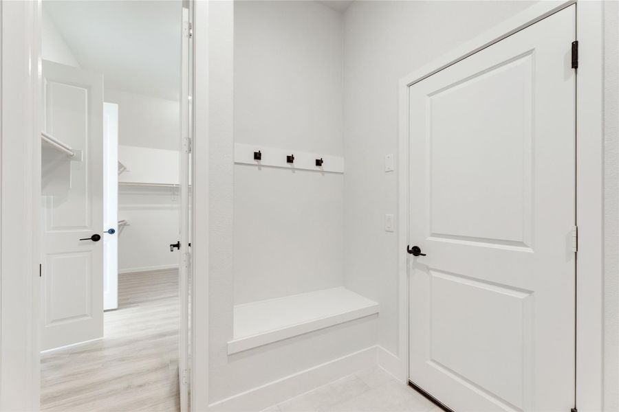 Mudroom with built-in bench, wall hooks, and light wood floors leading to a walk-in closet