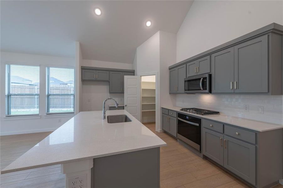 Kitchen featuring stainless steel microwave, a sink, gray cabinetry, tasteful backsplash, and light wood-style flooring